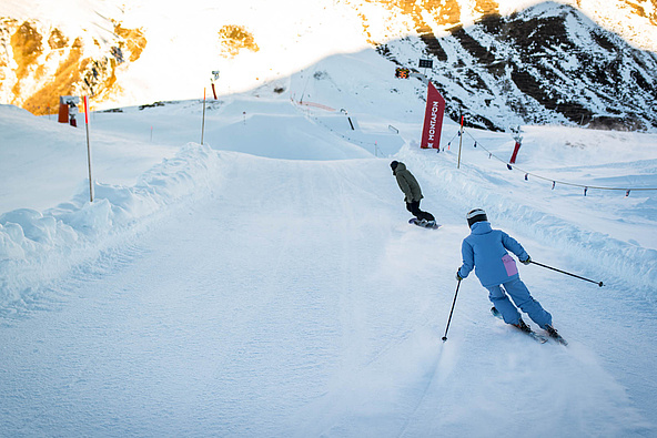 Ein Skifahrer und Snowboarder fahren auf Piste bergab