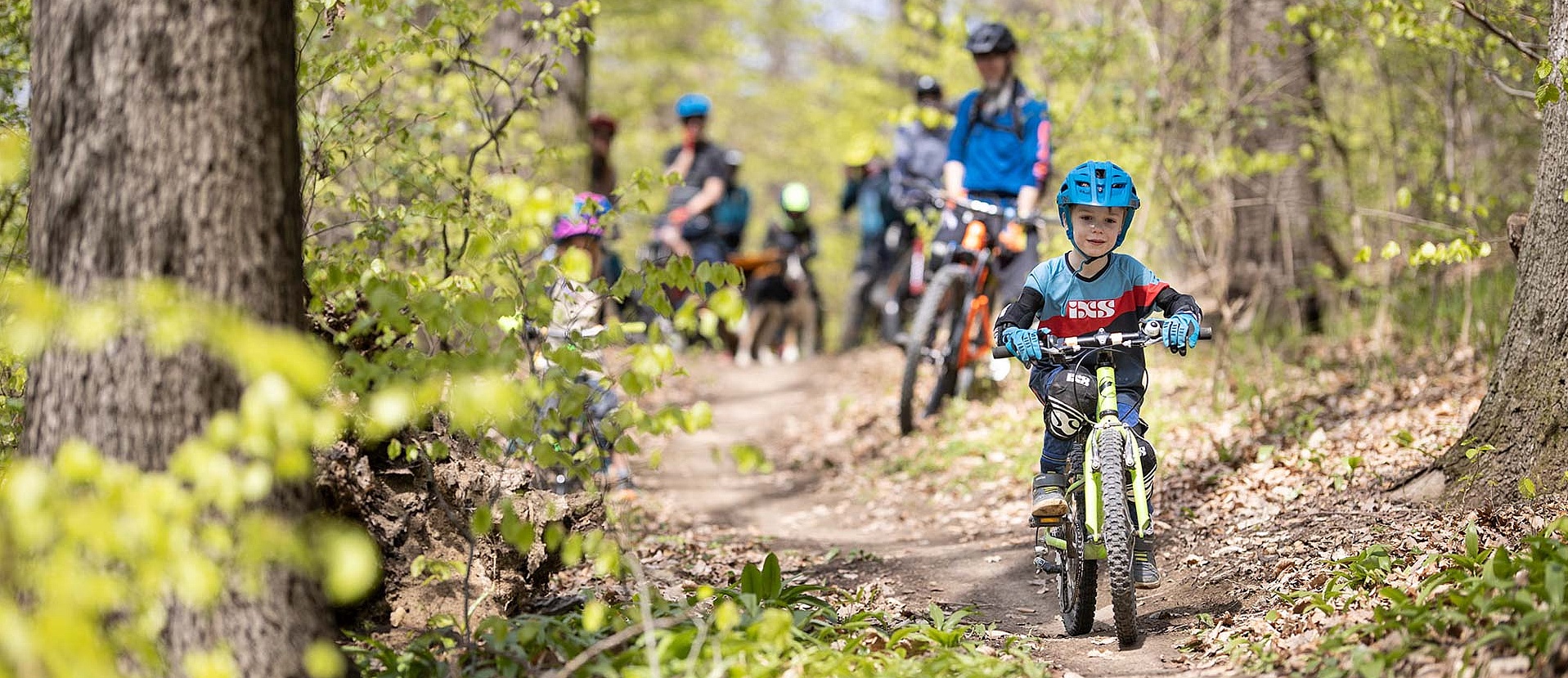 Child riding on easy trail in front of parents through autumn forestChild riding on easy trail in front of parents through autumn forest