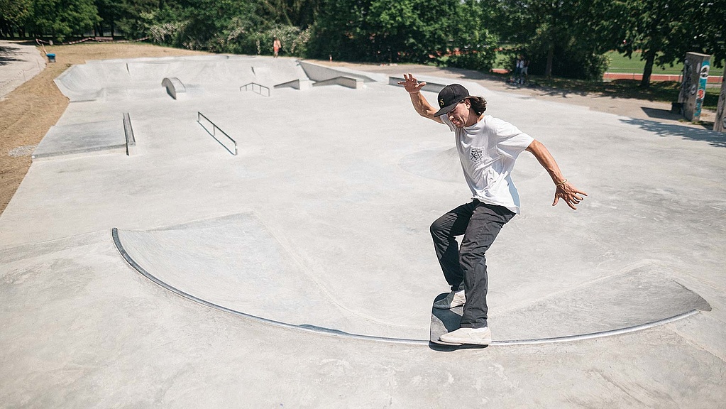 Skateboarder mit weißem T-Shirt macht einen Trick in einem Ortbeton Skatepark