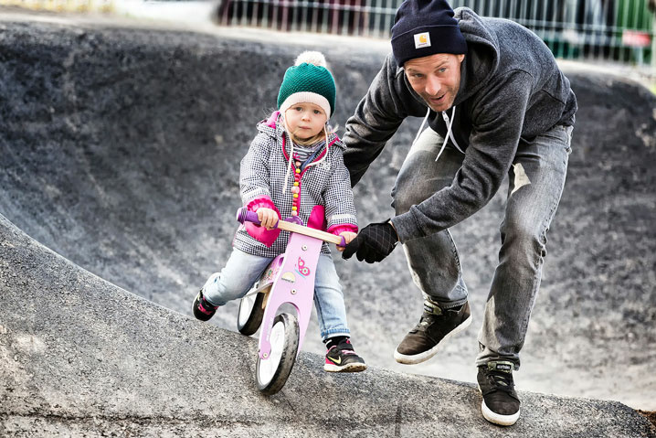 Vater schiebt seine Tochter auf einem Rosa Laufrad im Pumptrack