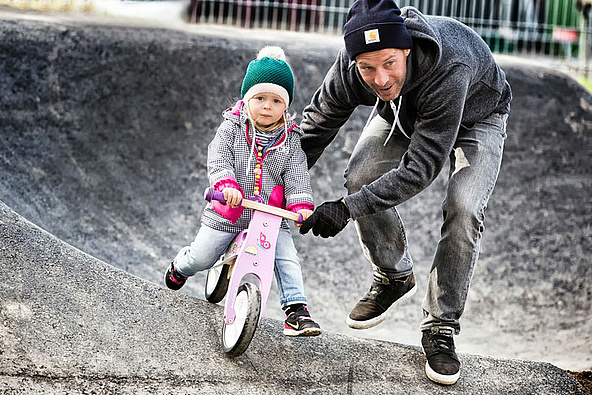 Father pushes his daughter on pink wheel in pumptrack