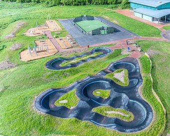 High-angle drone shot of a community sports park featuring a pumptrack, football pitch, playground, and sports hall.