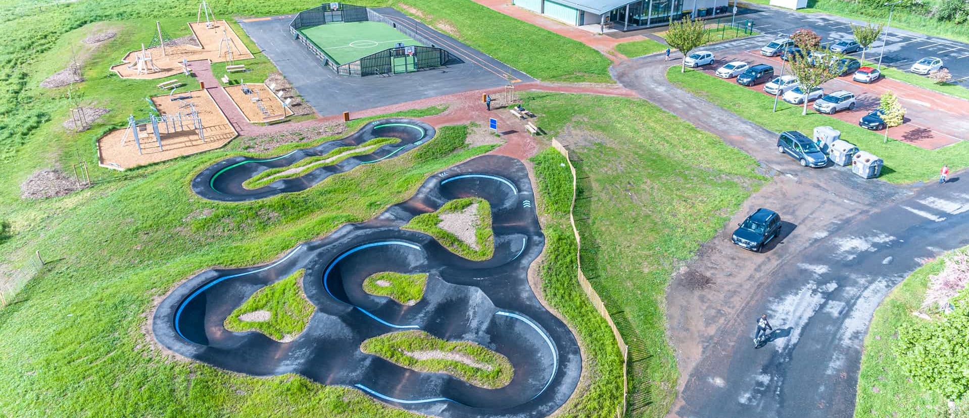 Vue aérienne par drone d'une aire de loisirs à Cublize comprenant un pumptrack, un terrain de sport et un gymnase.