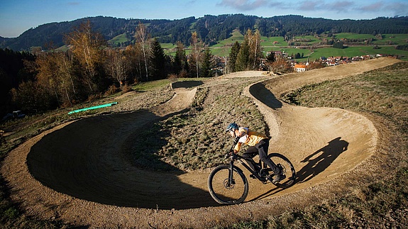 Mountain biker carving berm with view of Allgäu landscape at Bikepark Weitnau