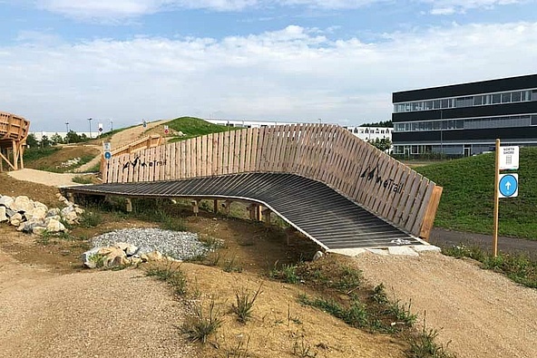 wooden obstacle bridge on e-bike trail in front of building