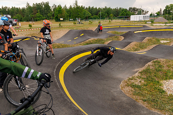 Urban Sports Park Bad Düben – viele Kinder und Jugendliche fahren auf dem Asphalt‑Pumptrack mit gelben Markierungen.