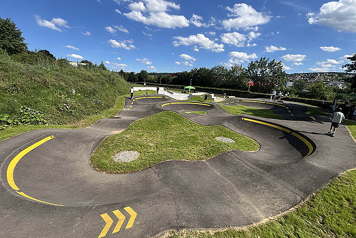 Pump track with curved asphalt lines and green grass islands at Urban Sports Park Uhingen