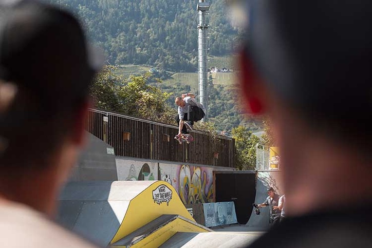 Blick über die Schultern von Zuschauern auf einen Skater, der einen Trick an der Rail-Kante vollführt.