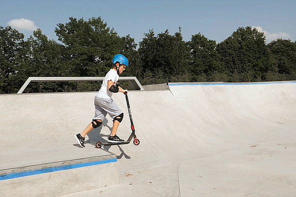 Child with scooter drives over heel in skate park