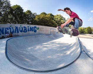 Skatepark Neuaubing Skateboarder mit rotem T-Shirt macht Trick in Ortbeton Skatepark