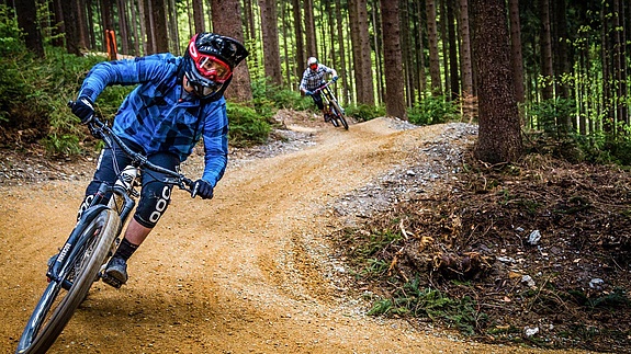 Two equipped bikers ride in the bike park in the forest