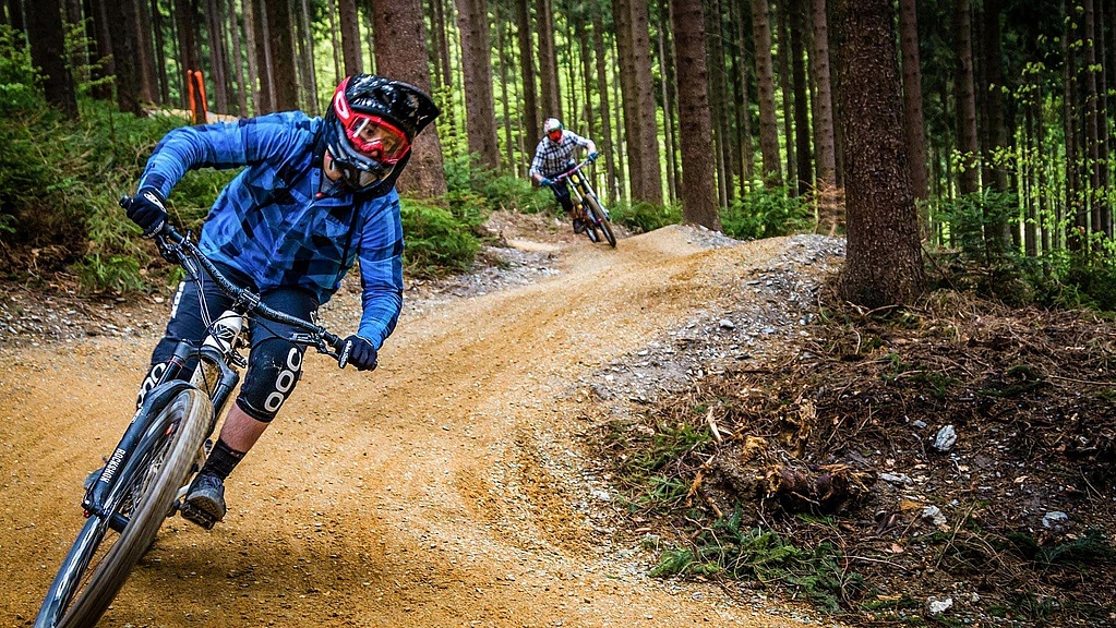 Two equipped bikers ride in the bike park in the forest