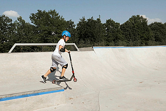 Kind mit Scooter fährt über Absatz im Skatepark
