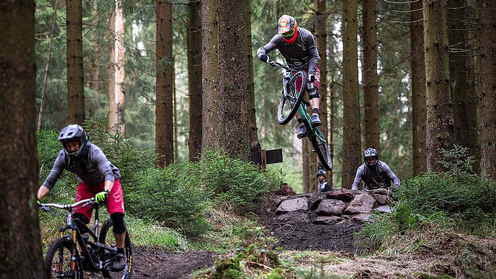 [Translate to Französisch:] Three bikers ride on challenging trail in forest