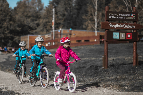 Three small children ride one after another on a gravel road