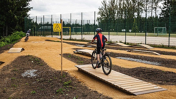 Mountain bikers practicing drop at MTB Park Rabenberg, yellow warning sign visible