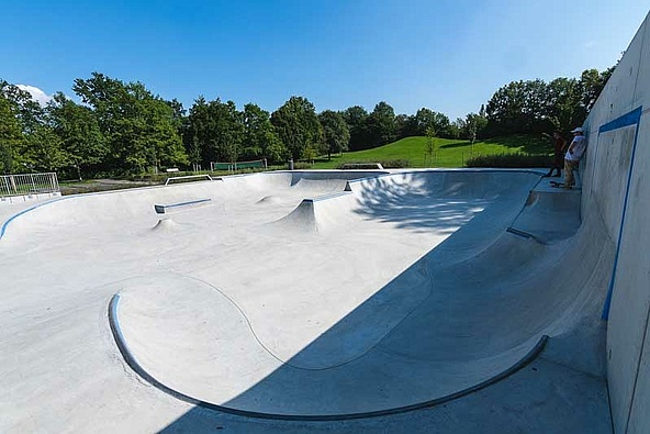 Blick auf leeren Ortbeton Skatepark mit Wiese und Bäumen im Hintergrund