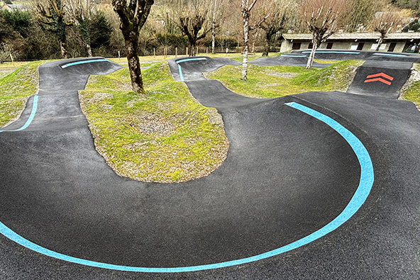 Nahaufnahme einer 180-Grad-Steilkurve mit blauer Führungslinie auf dem Pumptrack in Saint-Béat-Lez.