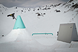 Snowboarder in der Luft mit einer Hand an einem großen türkisen Kegel
