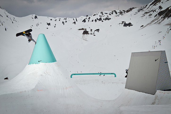 Snowboarder in the air with one hand on a large turquoise cone