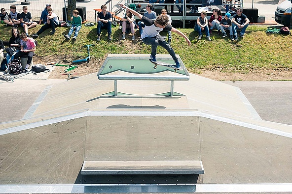 Skateboarder mit blau-weißem T-Shirt springt über eine Box in einem Skatepark