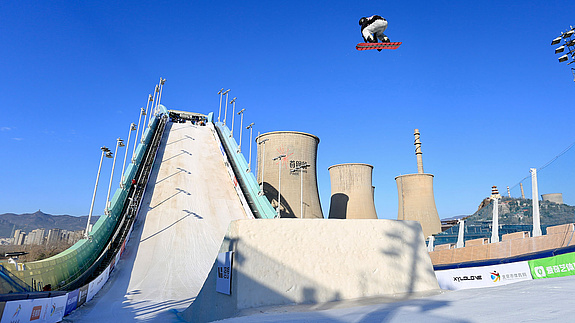 滑雪板运动员在首钢公园上空腾空而起，背景是冷却塔。