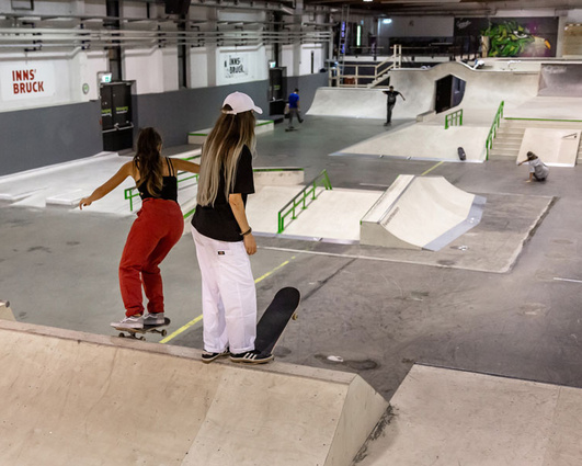 Two skateboarder at the Innsbruck indoor skatepark, surrounded by premium wood and concrete ramps.