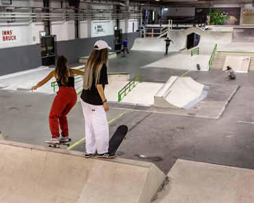 Two skateboarder at the Innsbruck indoor skatepark, surrounded by premium wood and concrete ramps.