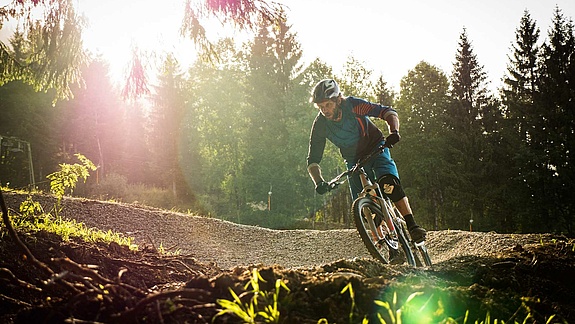[Translate to Chinesisch:] Mountain biker in a curve on a flow trail at the edge of the forest