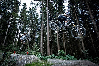 Two bikers jump on jump line in forest