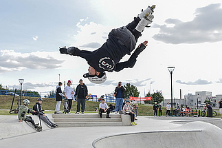 Inline-Skater zeigt spektakulären Backflip im Urban Sports Park Hückelhoven, Zuschauer sitzen am Beckenrand.