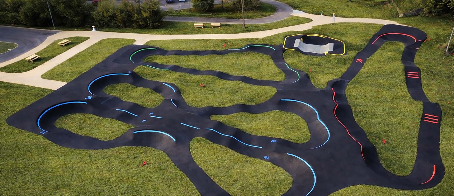 Große, moderne Pumptrack-Anlage in Lourdes mit asphaltierten Kurven und Wellen vor einer Kulisse aus Bäumen und bewaldetem Gelände.