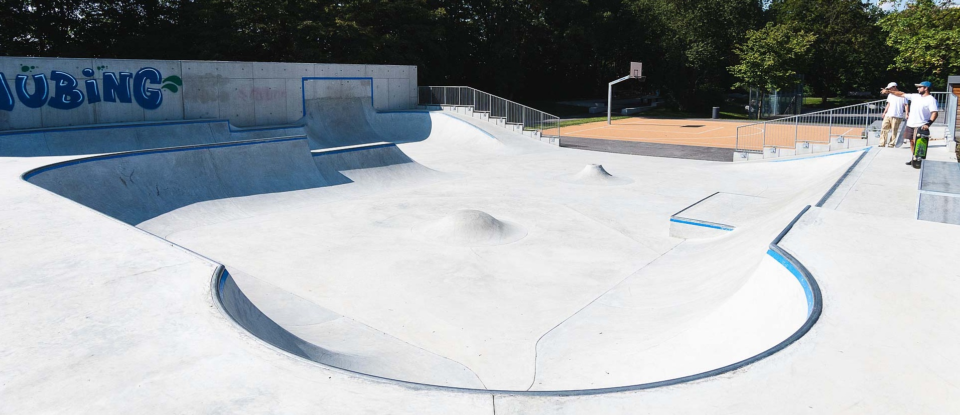 View of empty in-situ concrete skate park with basketball court in the background