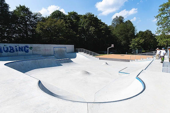 View of empty in-situ concrete skate park with basketball court in the background