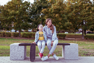 Mutter sitzt mit Kind und Skateboard auf einer Parkbank