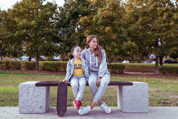 Mutter sitzt mit Kind und Skateboard auf einer Parkbank