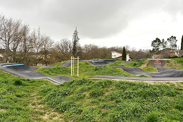 Piste vallonnée du pumptrack en asphalte à Saint-Geniès-Bellevue, entourée de pelouses vertes.