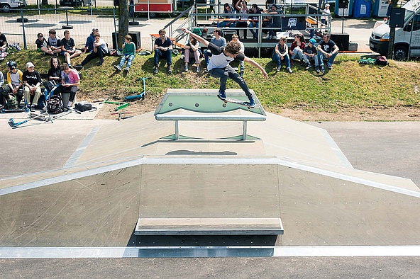 Skateboarder with blue and white T-shirt jumps over a box in a skate park