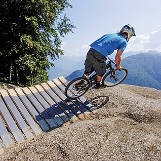 Biker jumps from north shore element in front of a forest