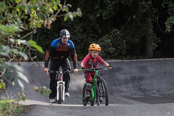 Adult and child ride MTB on asphalt pump track