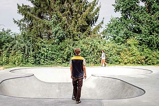 Skateboarder mit schwarzgelber Weste steht vor Ortbeton Bowl