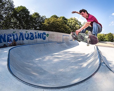 Skateboarder mit rotem T-Shirt macht Trick in Ortbeton Skatepark