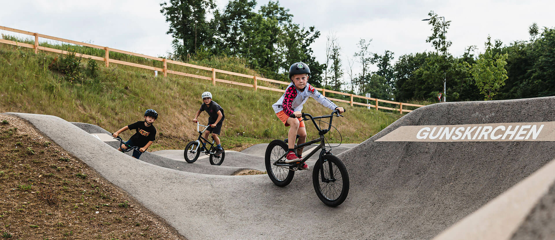 Three young boys ride their bike on pump track Gunskrichen