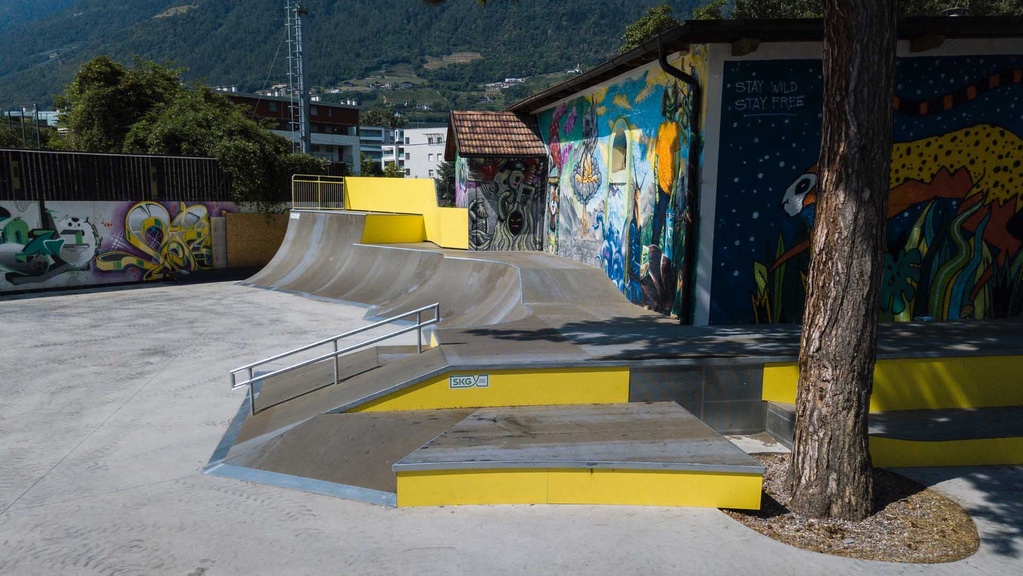 Beton-Quarterpipes und Rampen vor einer mit bunten Graffitis gestalteten Wand im Skatepark.