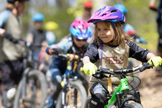 Mädchen sitzt auf Fahrrad mit Helm und weitere Biker im Hintergrund