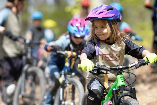 Mädchen sitzt auf Fahrrad mit Helm und weitere Biker im Hintergrund
