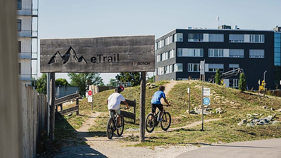 Office building behind entrance portal to the eTrail with two bikers 