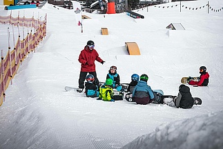 Snowboard Kindergruppe bekommt von einem Snowboardlehrer etwas erklärt