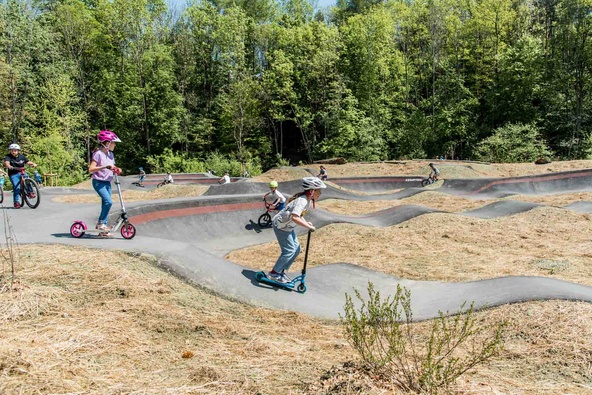Kinder mit Rollern und Rädern auf Pumptrack