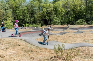 Kinder mit Rollern und Rädern auf Pumptrack